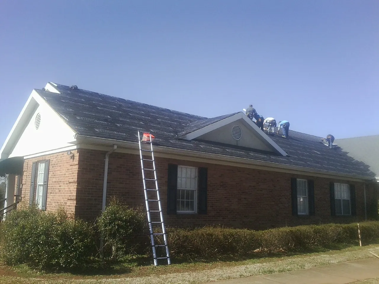 Crew tearing shingles off a brick ranch roof with a ladder set — Emergency Roof Repair work by our crew in Oley