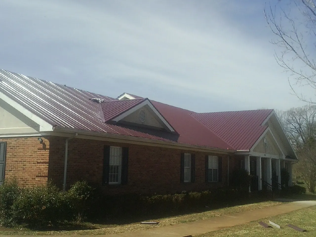 Red metal roof with gabled entries on a long brick building, from a Hail Damage Roof Repair job in Oley