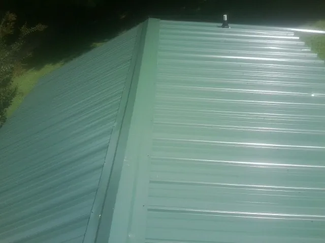 New green metal panels meeting at the ridge of a roof — Flat Roof Repair work by our crew in Oley